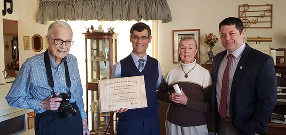 Four people in a living with notes on a wall and a museum benefactor holding a plaque.